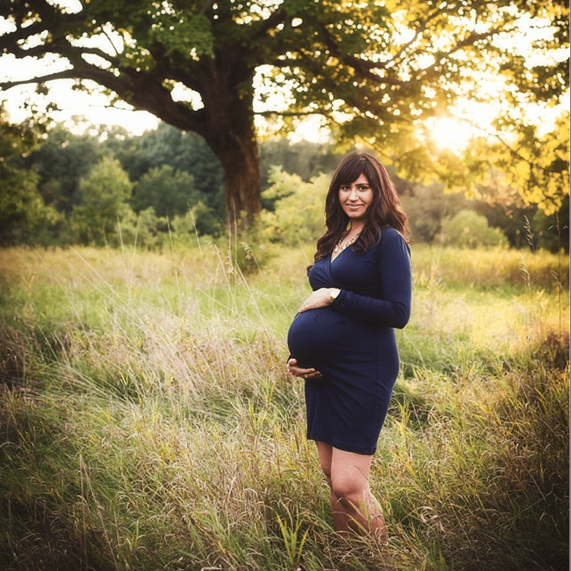 a pregnant woman standing in tall grass near a tree