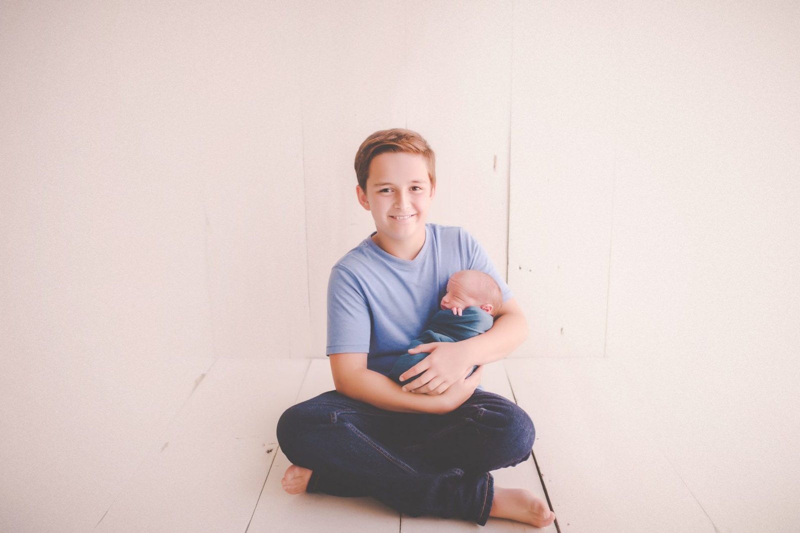 a young man sitting on the floor holding a baby