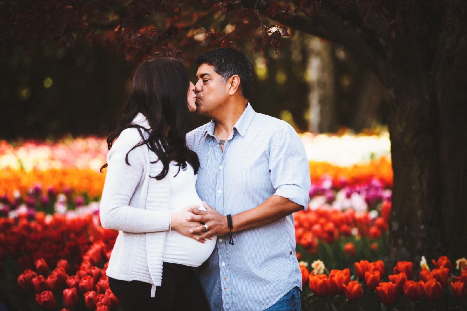 a pregnant couple kissing in front of colorful tulips