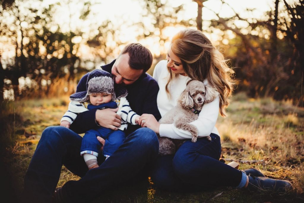a man, woman and child sitting on the ground with a dog
