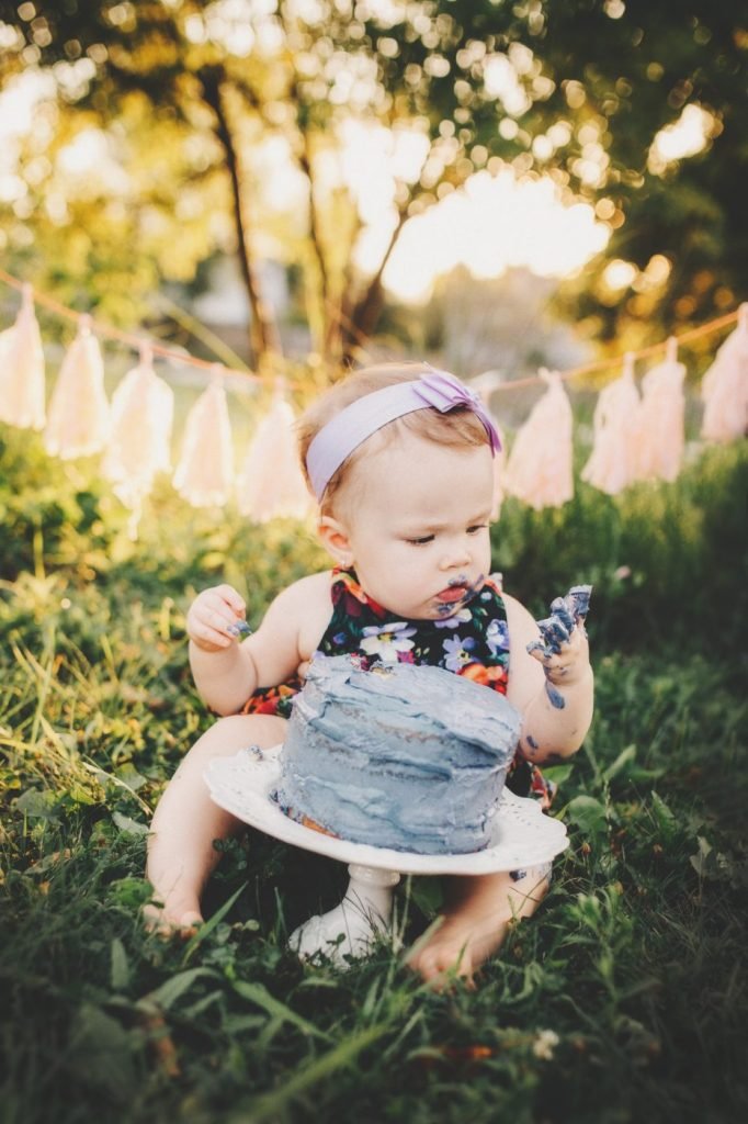 a baby girl sitting in the grass with a cake