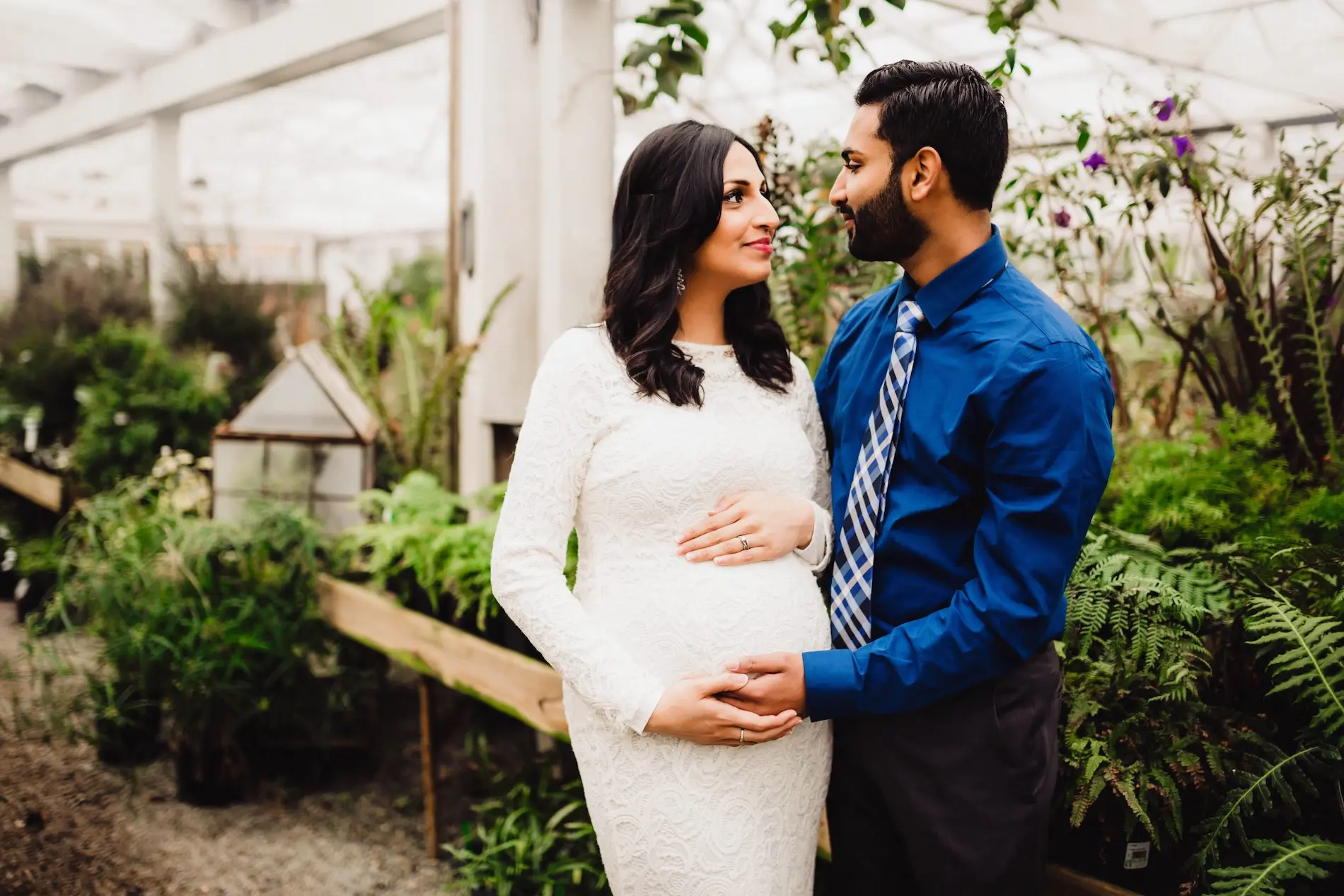 a pregnant couple standing next to each other in a greenhouse